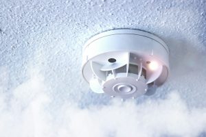 Smoke detector surrounded by haze symbolizing indoor smoke damage and odor cleanup