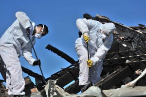 Restoration crew in protective suits cleaning up fire debris and damaged structure